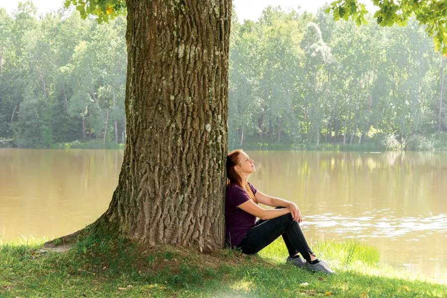 Jeune femme visiblement relaxée assise contre un arbre dans une forêt